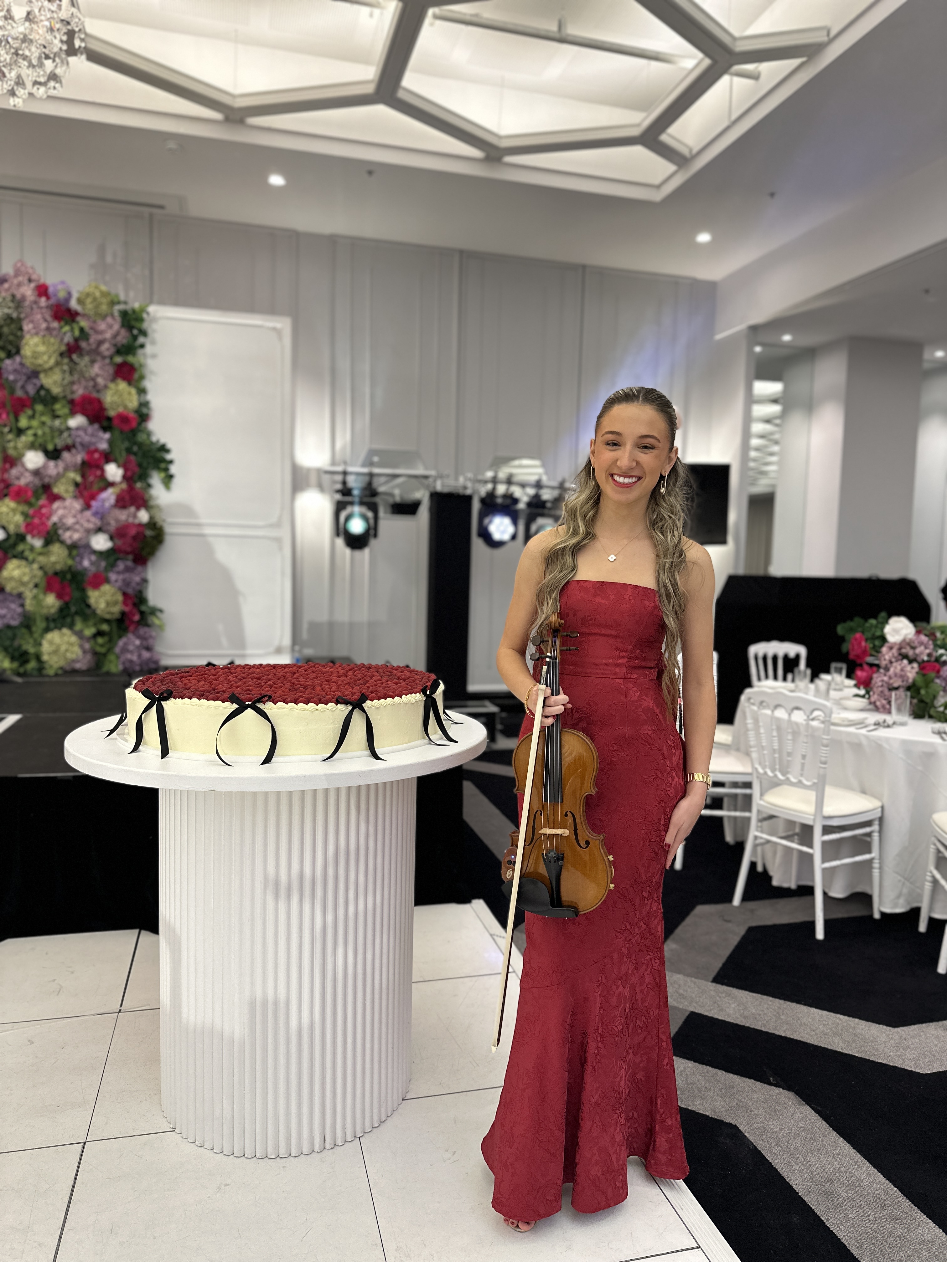 Tali in red dress standing next to large red cake